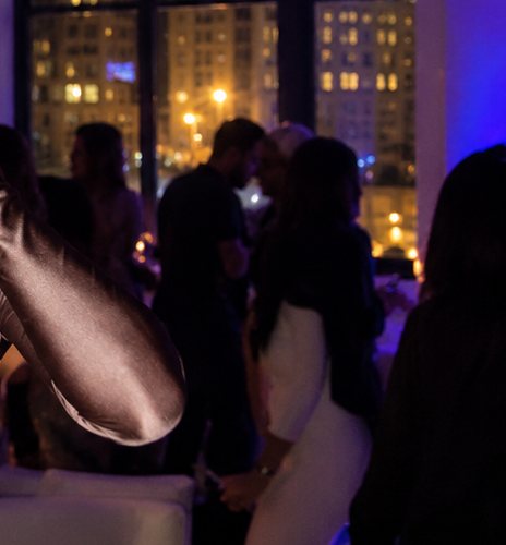 Guests in conversation with drinks, city lights through the windows behind them